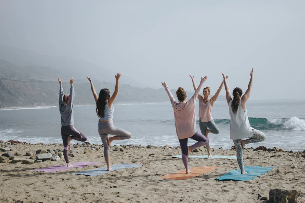 Five friends holding tree pose together on a beach