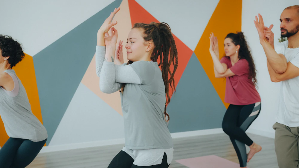 A teacher in a pink top leading a student through eagle pose in a bright studio
